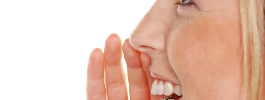 Jeune femme de profil, une main près de la bouche, qui murmure un secret en souriant