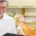 Homme aux cheveux gris en polo blanc tenant un dossier, patiente allongée au fauteuil dentaire derrière lui