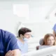 Praticien souriant en tenue bleue, bras croisés, et équipe soignante au fauteuil d'un cabinet dentaire