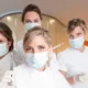 Quatre soignantes en blouse blanche et masque posant ensemble dans un cabinet aux murs bleus